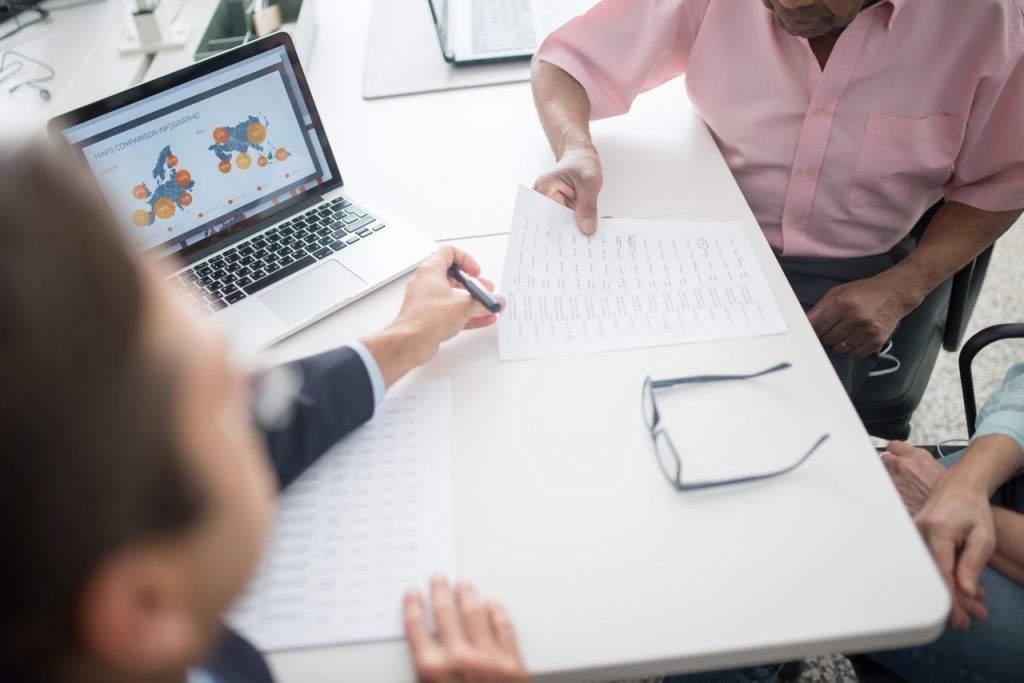 Senior couple reviewing documents with consultant at office desk with laptop.